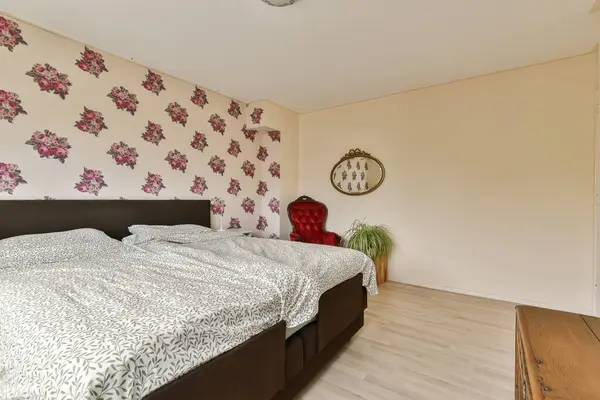 a bedroom with floral wallpaper on the walls and wood flooring in front of the bed, there is a mirror hanging above