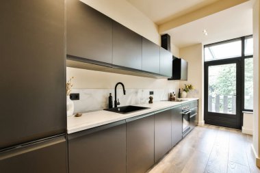 Bu küçük alanda siyah dolapları ve beyaz tezgahları olan modern bir mutfak eğlenmek için idealdir.