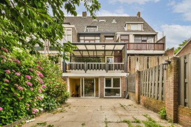 Evin önünde tuğladan duvarlar ve yeşil bitkiler büyüyen bir ev manzarası.