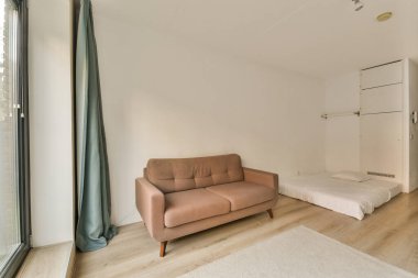 Arka plandaki verandaya açılan kanepesi, yatağı ve sürgülü kapısı olan bir oturma odası.