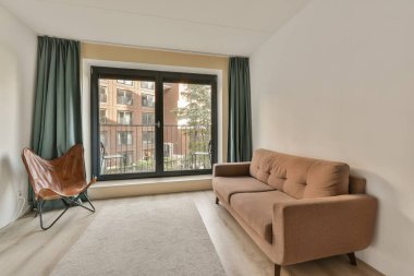 Oturma odası, kanepe, sandalye ve geniş pencereli. Evin önündeki sokağa bakıyor.