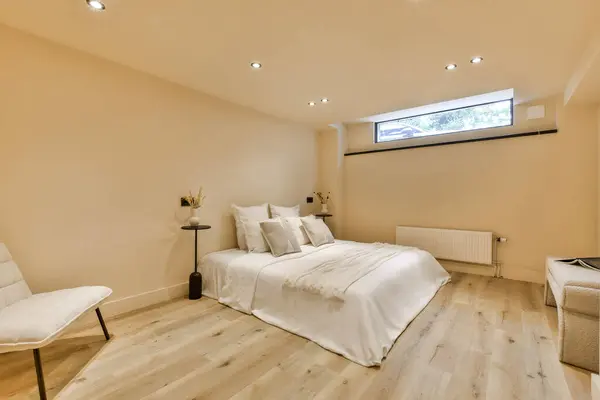 a bedroom with wood flooring and white bedding in the middle of the room, there is a large window