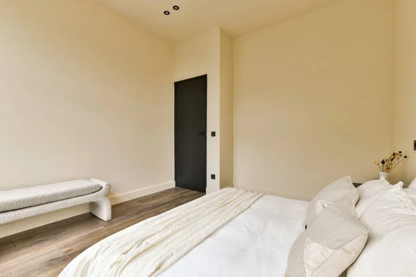 a bedroom with wood flooring and white sheets on the bed, there is a black door in the room
