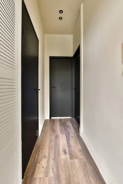a long hallway with wood floors and black doors on either side by side, leading to the other areas in the room
