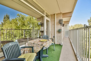 Sandalyeli bir teras ve evin önündeki çimlerin üzerinde bir masa, açık mavi gökyüzü.