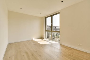 Boş bir oda, ahşap döşemeli ve geniş pencereli şehir merkezlerine bakan.