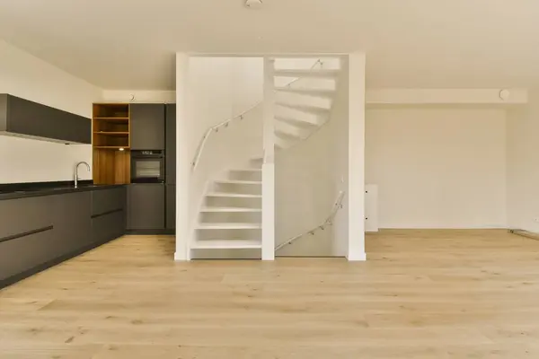 a kitchen and stairs in a room with white walls, wood flooring and black cabinetd cupboards on either side