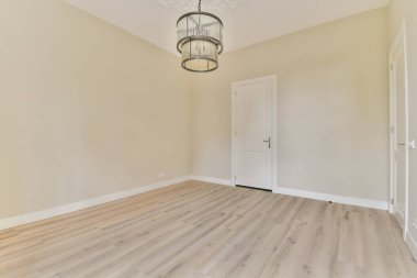 Geniş, minimalist bir oda. Açık renkli duvarlar, ahşap bir zemin ve şık bir avize. Huzurlu ve davetkar bir atmosfer yaratıyor..