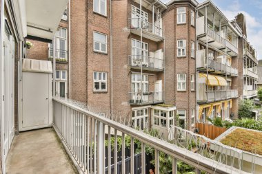 Modern bir apartman balkonundan manzaralı bir manzara klasik tuğla mimarisini ve aşağıdaki manzaralı bahçeleri sergiliyor, sakin bir kentsel atmosfer yaratıyor..