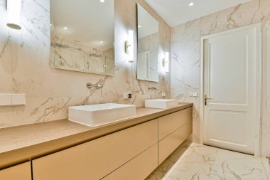 Mermer duvarlar ve zarif aksesuarların bulunduğu geniş, modern bir banyo. Zarif ve sofistike bir ortam sağlıyor. Tasarım rahatlığı ve minimalizmi vurguluyor..