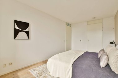 Sakin ve minimalist bir yatak odası. Tarafsız renkler, basit mobilyalar ve duvarda sanat eserleri, sakin ve davetkar bir atmosfer yaratıyor..