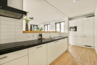 İçinde minimalist dolaplar, siyah bir tezgah ve geniş pencerelerden bol miktarda ışık bulunan çağdaş bir mutfak. Temiz hatlar geniş ve davetkar bir atmosfer yaratıyor..