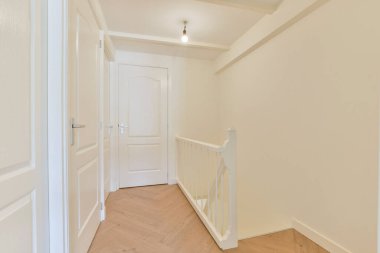 Temiz çizgiler, beyaz duvarlar ve parlak ahşap döşeme içeren parlak, minimalist bir koridor. Tasarım basitliği ve zarafeti vurgular..