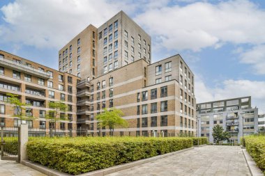 Bulutlarla benekli mavi gökyüzü ile tamamlanmış çağdaş bir konut kompleksi gösterişli zarif mimari ve yeşillik.