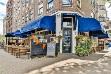 Mavi gölgelikler, ahşap masalar ve renkli dekorasyonlarla dolu canlı bir açık hava kafesi rahatlama ve yemek için davetkar bir ortam yaratıyor..