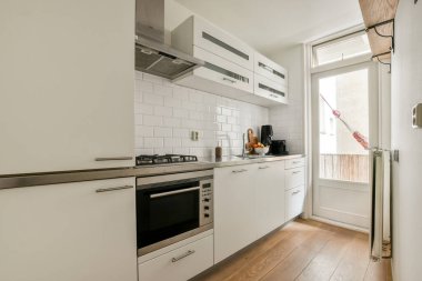 Beyaz dolapların, paslanmaz çelik aletlerin ve geniş bir yerleşimin olduğu çağdaş bir mutfak. Doğal ışık odayı dolduruyor, modern estetiğini geliştiriyor..