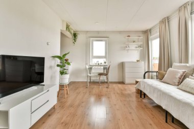 Parlak ve havadar oturma odasında modern minimalist tasarım sergileniyor. Hafif ahşap döşeme ve rahat bir estetik için basit mobilyalar..