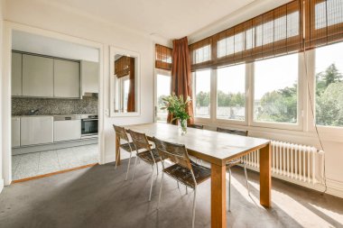 Şık sandalyelerle çevrili ahşap bir masa ve geniş pencereli, doğal ışık ve açık hava manzarası olan gösterişli bir yemek salonu..