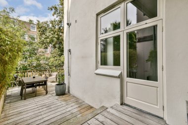 Çağdaş bir balkon, ahşap süsleme, saksı bitkileri ve bir yemek masası, yeşil ve doğa ile çevrili sakin bir açık hava alanı sağlar..