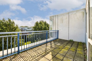 Temiz bir tasarıma sahip modern bir balkon, yemyeşil ve açık mavi gökyüzüne bir bakış sunuyor, sakin bir açık hava deneyimini davet ediyor..