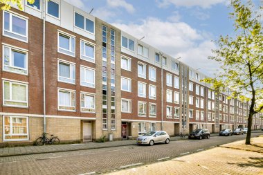 Yeşillik ve park halindeki arabalarla çevrili, birden fazla penceresi olan modern bir apartman. Kentsel yaşam için ideal.