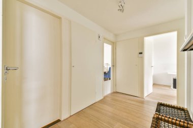 Açık renkli duvarlar, ahşap döşemeler ve davetkar bir atmosfer içeren ferik ve minimalist bir iç koridor. Kapılar farklı odalara açılıyor, erişilebilirliği arttırıyor..