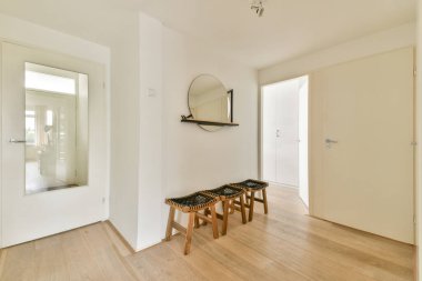 Gösterişli ve modern bir koridorda minimalist tasarım elementleri, açık ahşap döşemeler ve yuvarlak ayna aksanı var. Mekan parlak ve havadar, sadelik sergiliyor..