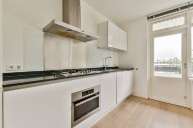 Paslanmaz çelik aletlerin, beyaz dolapların ve doğal ışığa izin veren açık bir pencerenin olduğu şık, modern bir mutfak. Minimalist tasarım işlevselliği vurgular.