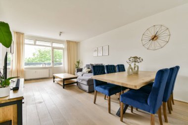 Rahat bir kanepe, zarif bir yemek masası ve mekanı doğal ışıkla aydınlatan büyük pencereli modern ve şık bir oturma odası..