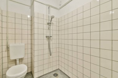 Beyaz fayanslı duvarlar, parlak bir duş başlığı ve minimalist estetiği somutlaştıran basit bir temizlik ünitesi olan çağdaş bir duş alanı..