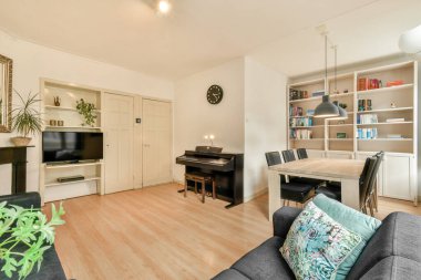 Modern oturma odasında şık bir kitaplık, zarif bir piyano ve rahat bir oturma düzeniyle rahatlamak ve okumak için mükemmel bir zaman..