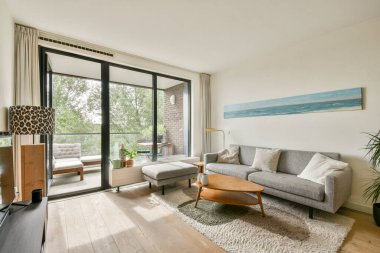 Tarafsız bir kanepe, geniş pencerelerden geçen doğal bir ışık ve hoş bir atmosfer yaratan samimi dekorların olduğu modern bir oturma odası..