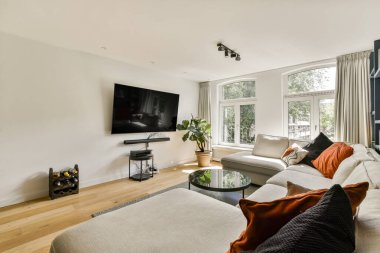 Geniş bir televizyon, zarif bir oturma odası ve geniş pencerelerden yayılan geniş doğal ışık, rahat bir ortam yaratıyor..