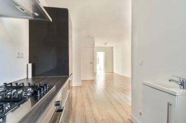 Paslanmaz çelik aletler ve ahşap döşeme ile donatılmış şık, modern bir mutfak, iyi aydınlatılmış bir koridora açılıyor. Tasarım minimalizmi ve boşluğu vurguluyor..