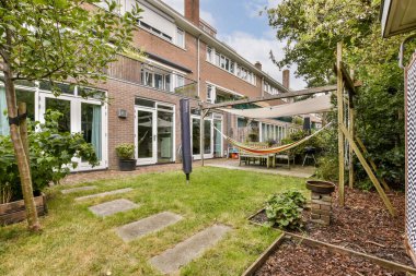 Arka planda yemyeşil ve şık mimari ile çevrili, bir hamağa uzanan taştan bir patika içeren huzurlu, modern bir bahçe..