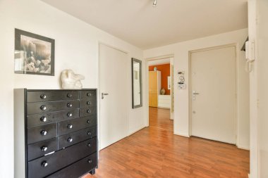 Gösterişli bir giriş salonu, koyu ahşap döşeme, minimalist dekor ve zarif bir zarafet. Uzay, siyah bir elbise ve çerçeveli bir sanat içeriyor. Hoş bir atmosfer yaratıyor..