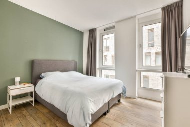 Geniş ve şık bir yatak odası, yeşil ve beyaz duvarlar, bol doğal ışık ve rahatlatıcı bir atmosfer için çağdaş mobilyalar..