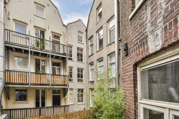 Balkonları olan bitişik konut binalarının yer aldığı bir manzara, şehir ortamında kentsel mimari ve yeşillik vurgulanıyor.