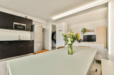 Çağdaş bir mutfak, gösterişli bir dolap, bir yemek masası ve bol miktarda doğal ışık. Tasarım açık alan ve minimalist dekor vurguluyor.
