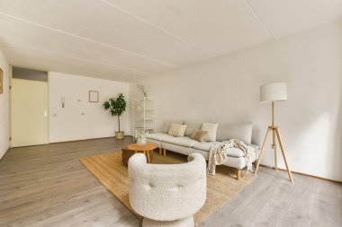 Minimalist mobilyaların, rahat bir halının, yeşilliğin ve sıcak ışığın bulunduğu güzel tasarlanmış modern bir oturma odası rahatlatıcı bir atmosfer yaratıyor..