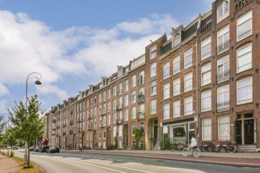 Tarihi tuğla binalar, bisikletler ve sakin mavi gökyüzüyle kaplı büyüleyici bir Amsterdam caddesinin manzarası. Atmosfer şehirlerin eşsiz mimarisini yansıtıyor..