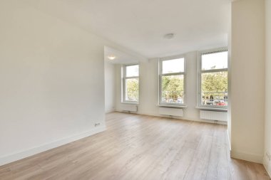 Boşluğu doğal ışıkla dolduran, temiz çizgiler ve taze bir hisle donatan geniş pencereli davetkar boş bir oda..