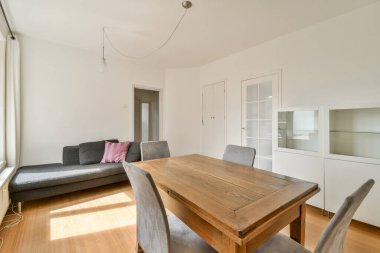 Ahşap bir masa ve şık koltukların olduğu minimalist, modern bir oturma odası. Doğal ışık içeri akar, sıcak ve davetkar bir atmosfer yaratır..