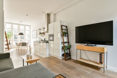 Rahat bir oturma alanı, doğal ışık için geniş pencereler ve modern mobilya tasarımına sahip modern bir yaşam alanı. Rahatlamak ve sosyalleşmek için ideal.