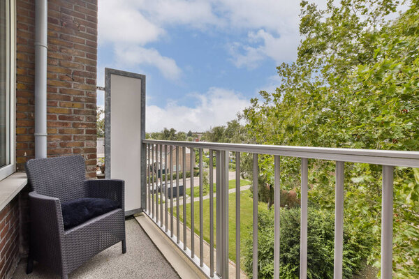 A contemporary balcony featuring a comfortable chair and a lush green landscape filled with trees and blue sky. Ideal for relaxation and enjoying nature.