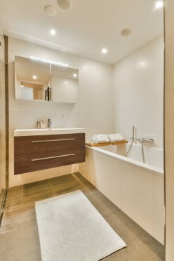 Ahşap bir kibrin, büyük bir aynanın ve küvetin olduğu gösterişli modern bir banyo. Minimalist tasarım, temiz çizgileri ve nötr renk paletini vurgular..