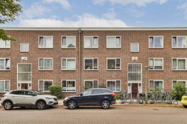 Benzersiz bir cephesi ve birden fazla penceresi olan modern bir bina. Ön planda park halindeki araçlar ve bölgeyi çevreleyen yeşillikler tarafından tamamlanmış..