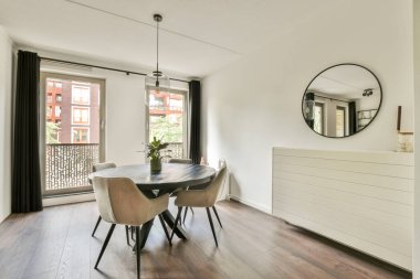 Yuvarlak bir masa, rahat sandalyeler ve çağdaş dekor ile tamamlanmış balkon kapılarından geniş doğal ışık içeren şık bir yemek odası..