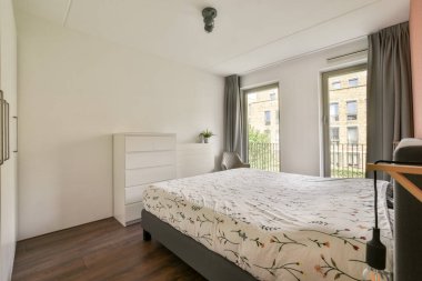 Minimalist bir tasarıma sahip çağdaş bir yatak odası, geniş pencerelerden bol miktarda doğal ışık ve konfor ve estetik için şık mobilyalar..