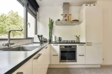 Beyaz dolaplar, paslanmaz çelik aletler ve büyük pencerelerden yeşillik manzarası olan gösterişli, modern bir mutfak. Mutfak ilhamı için mükemmel..